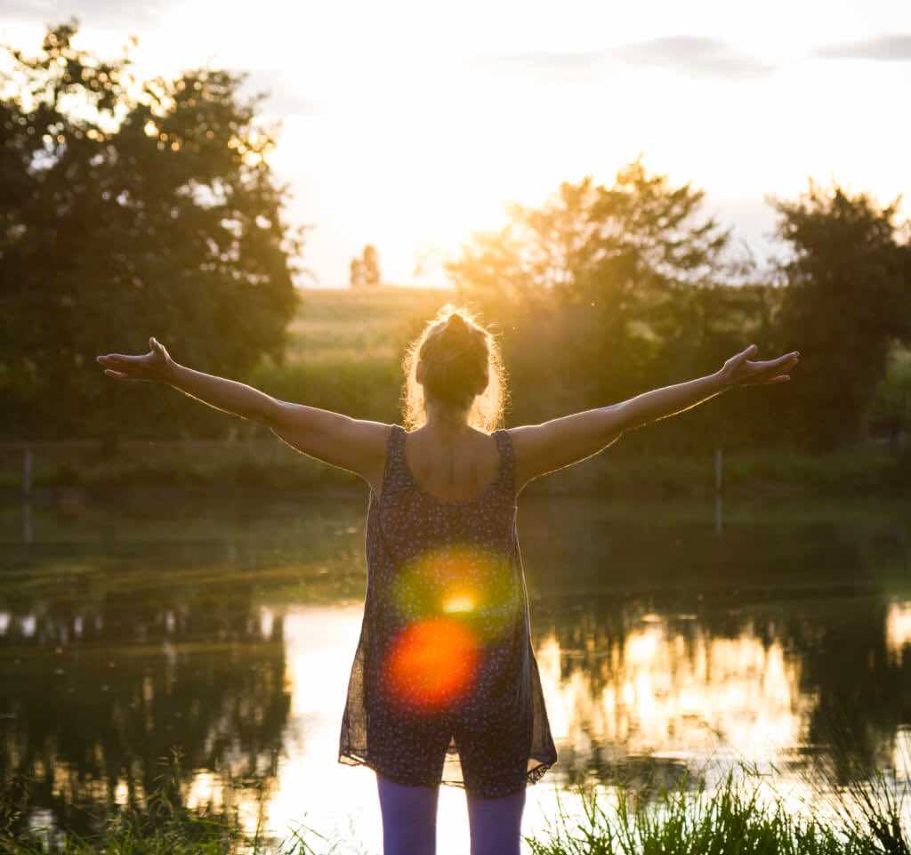 Woman standing with arms wide open in front of a lake