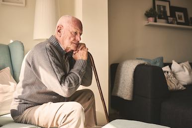 Old man sitting on a couch and holding a cane feeling lonely