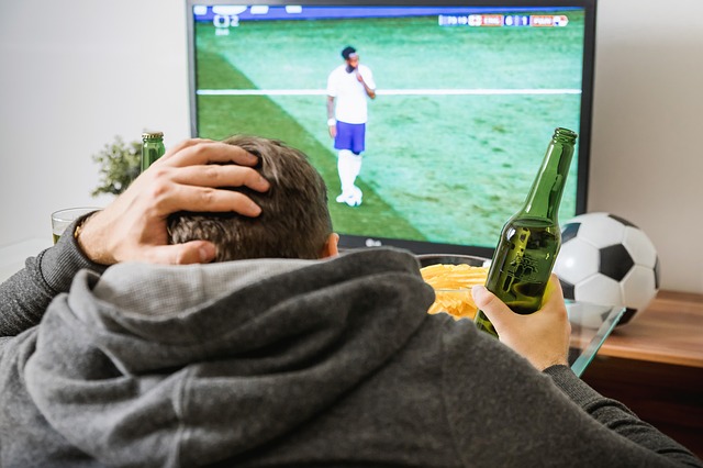 Man sitting on a coach holding a beer wile watching a soccer game on tv